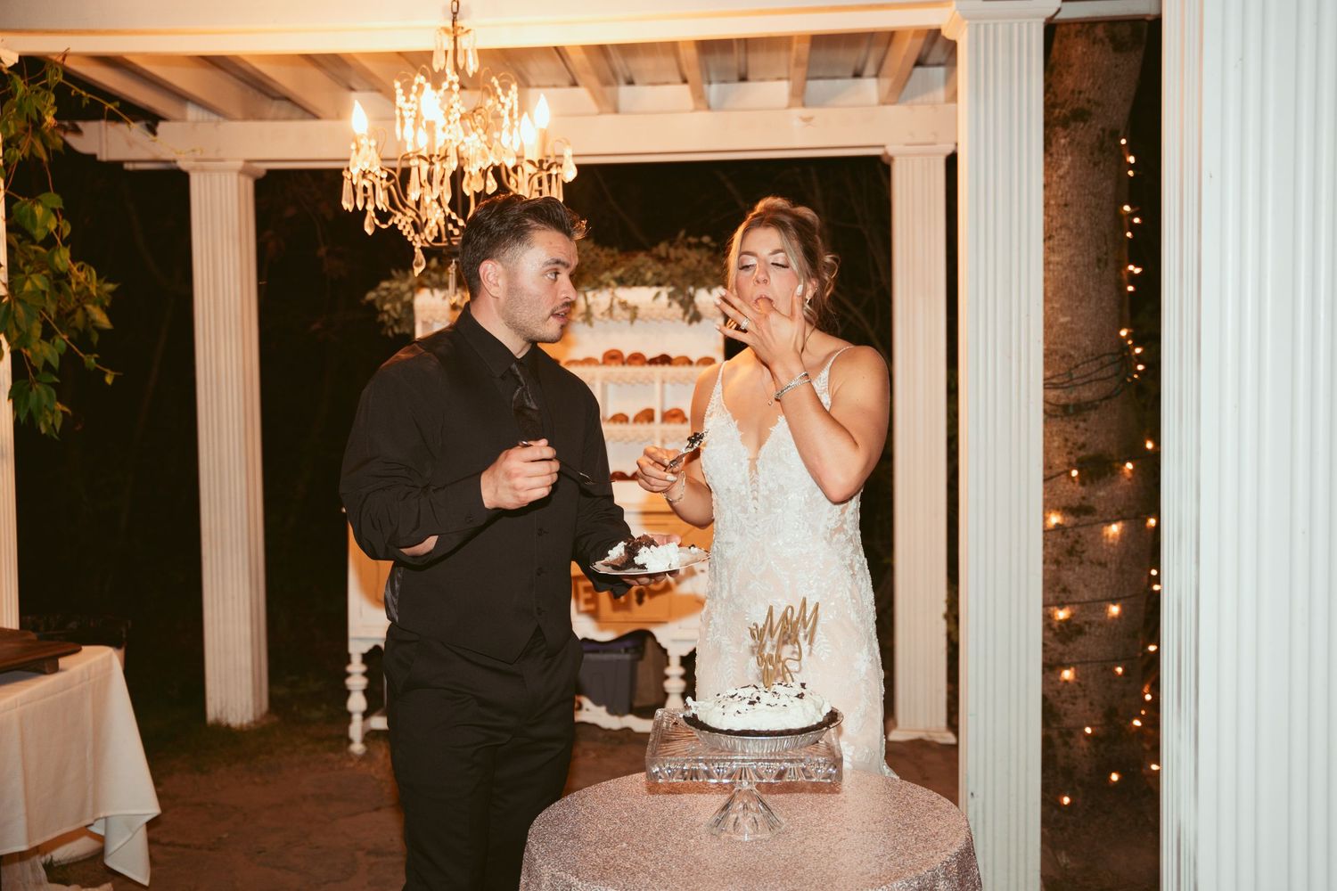 A couple sharing a moment at their wedding cake table under elegant lighting.