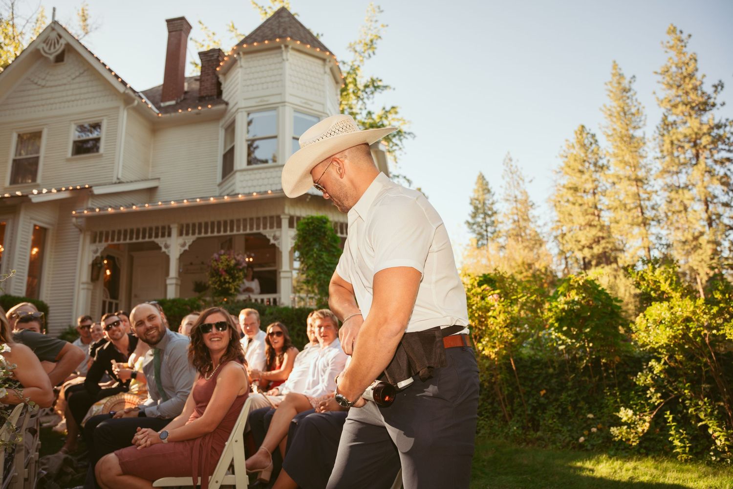 Entertainer performs for seated wedding guests in front of Victorian-style house at sunset.