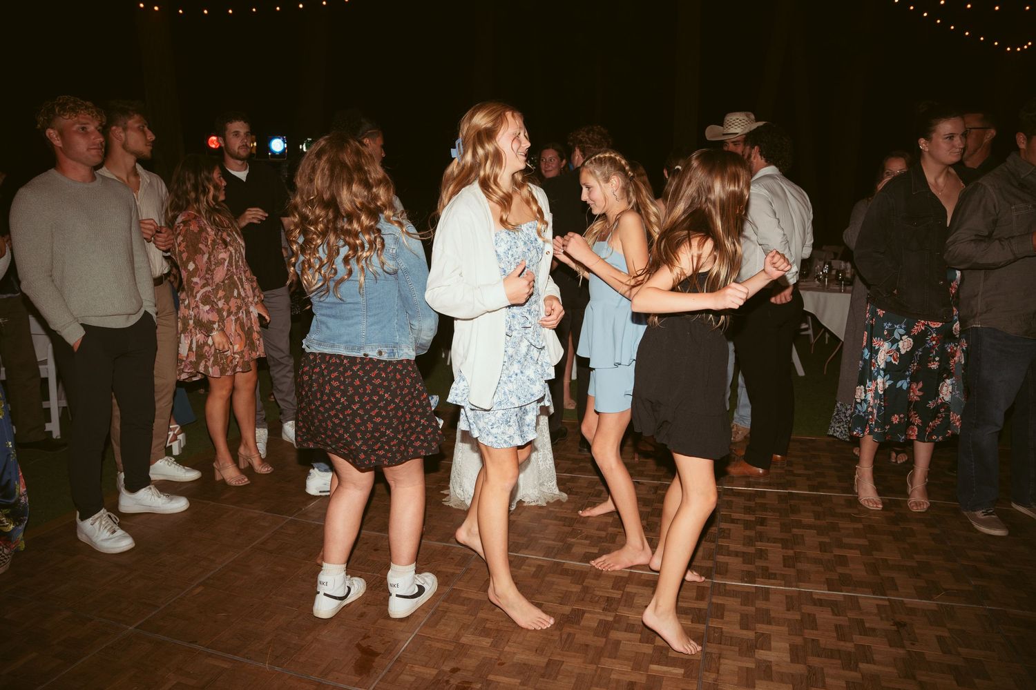 Wedding party dancing energetically on a wooden dance floor during an outdoor evening celebration.