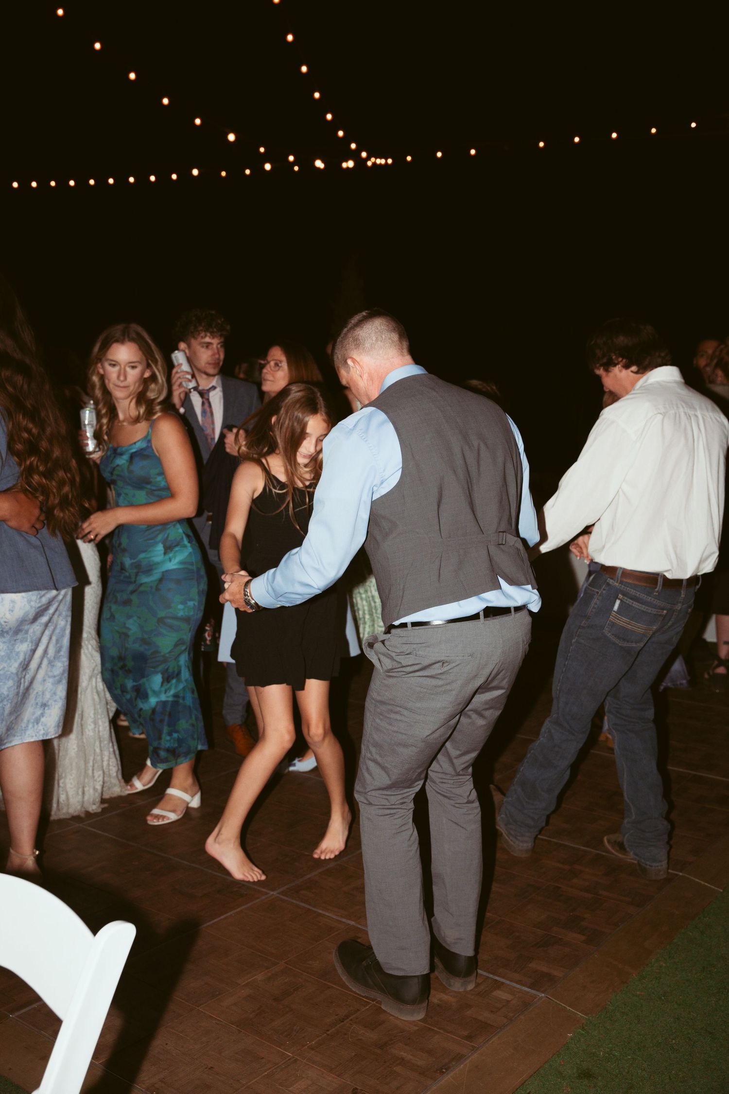 People dancing on a patio floor during an evening celebration with string lights above.