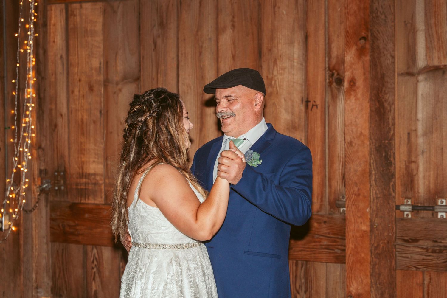 A couple dances together in a rustic wooden barn setting with twinkling lights.