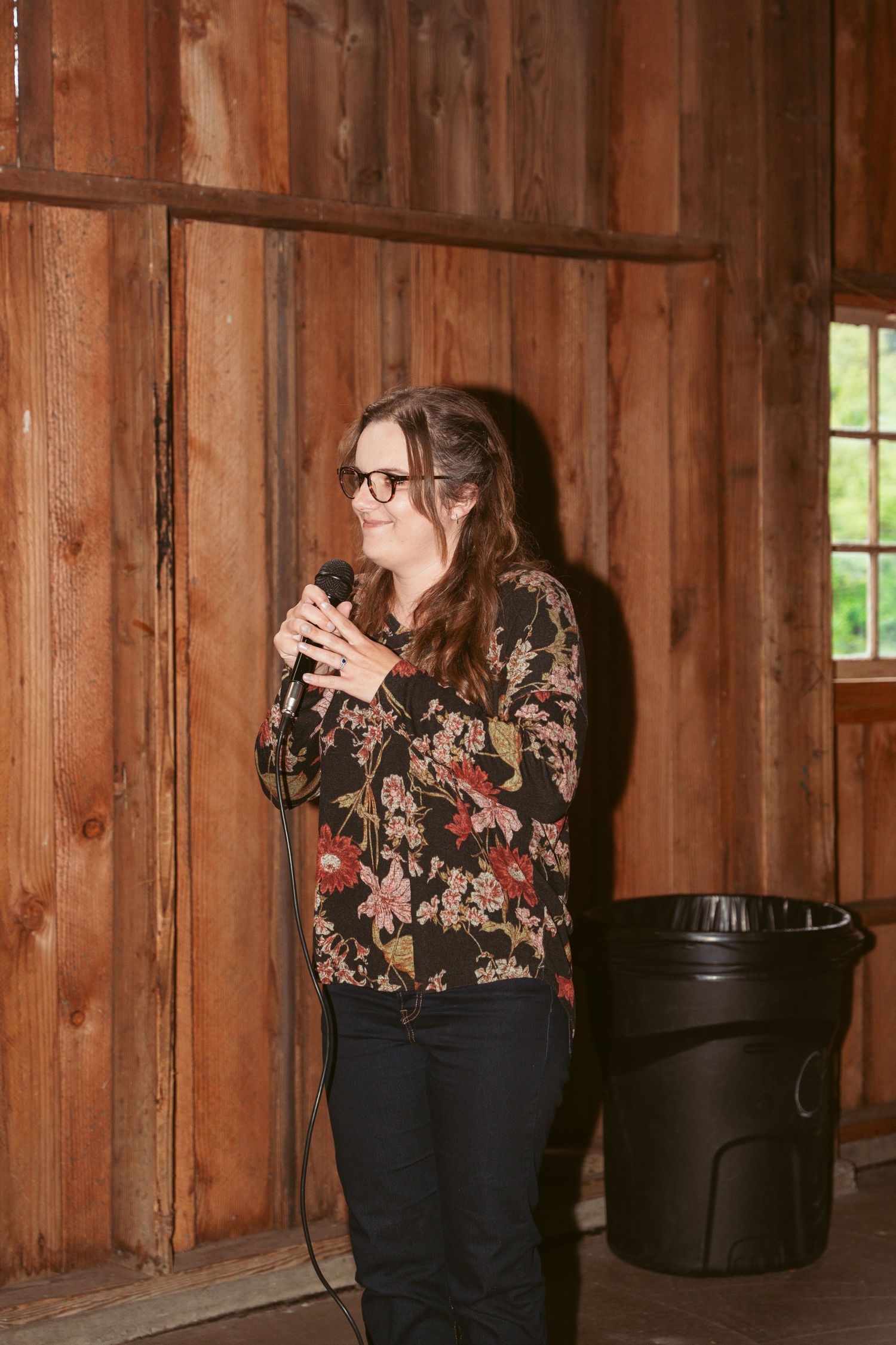 Person in formal attire poses inside a rustic wooden barn setting with natural window light.