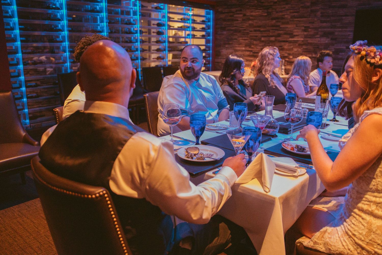 Wedding reception party scene with guests dancing under blue lighting and brick walls.
