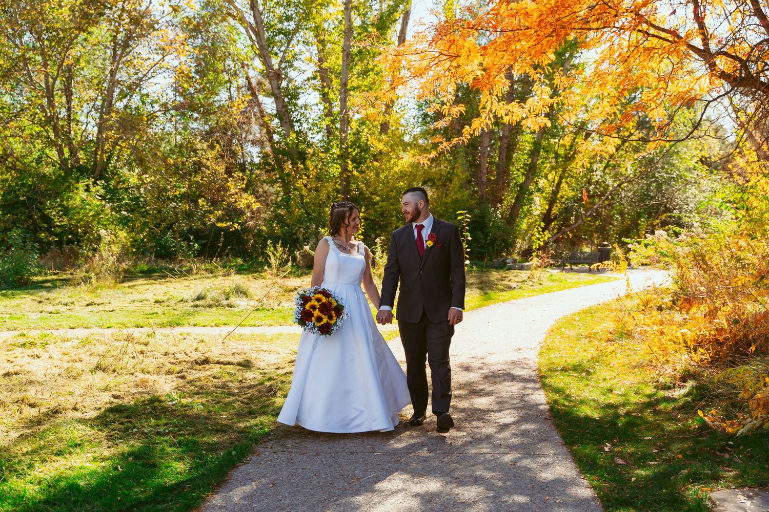A couple walks along a winding autumn path surrounded by vibrant yellow and orange foliage.