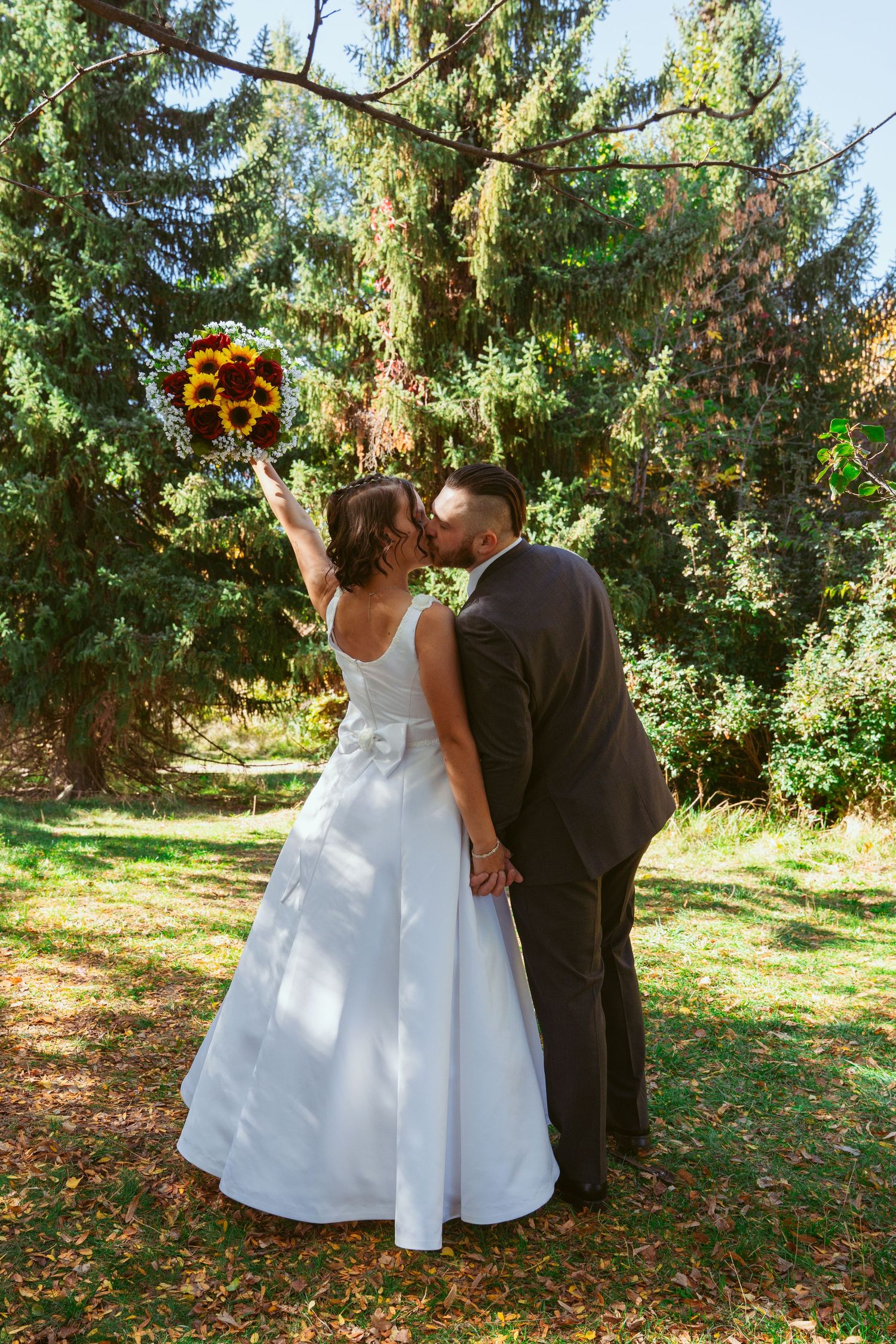 Wedding couple shares intimate moment under evergreen trees in autumn setting.