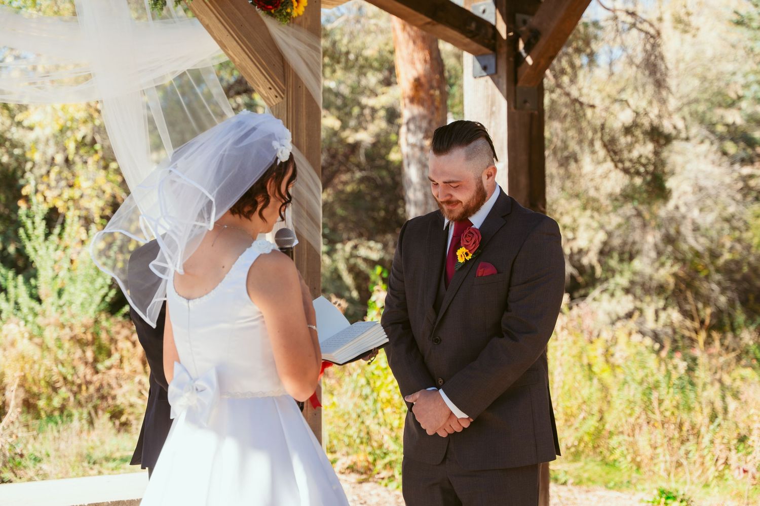 Intimate wedding ceremony moment under wooden pavilion decorated with autumn flowers.
