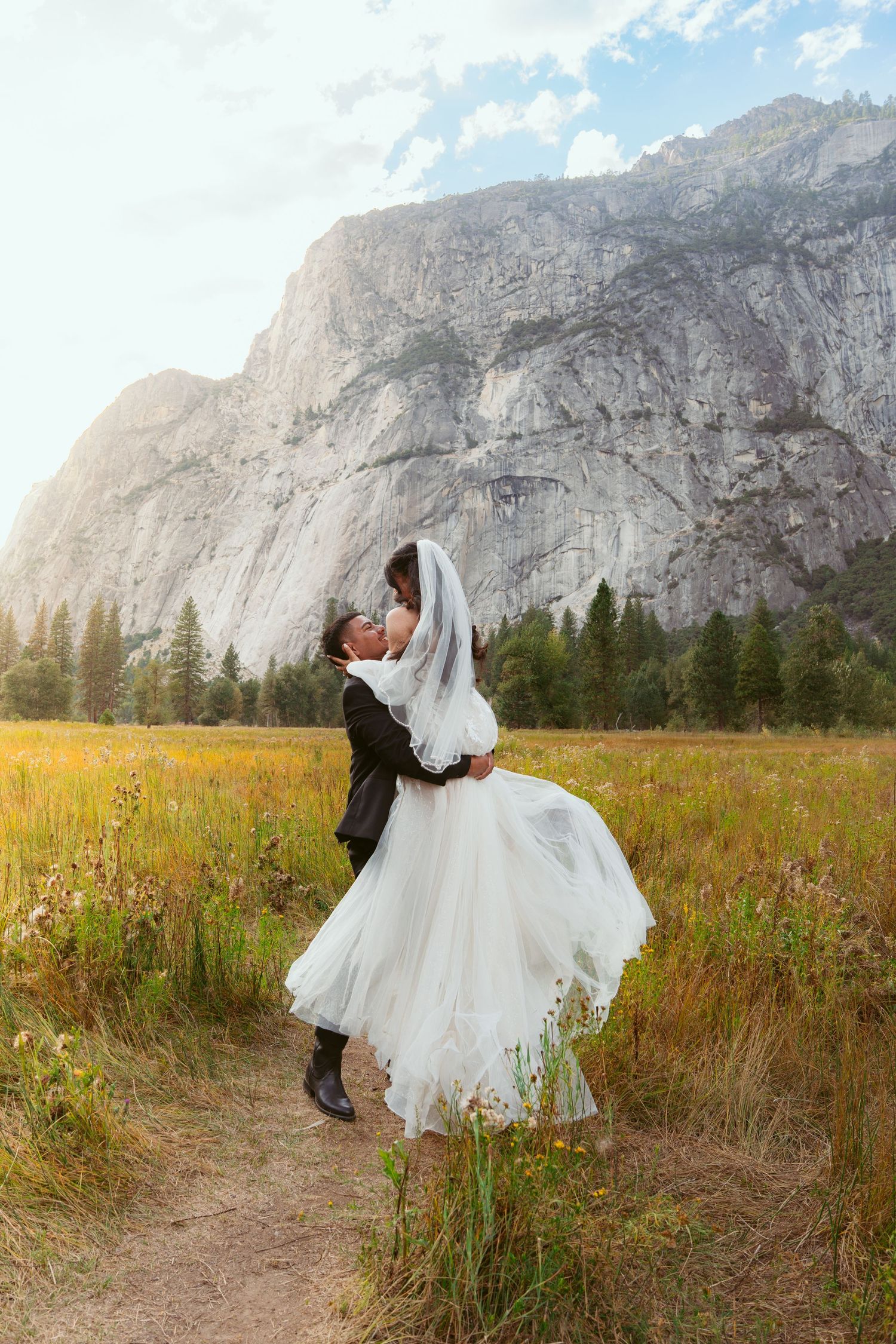 Newlyweds share a romantic moment in Yosemite Valley with Half Dome in the background.