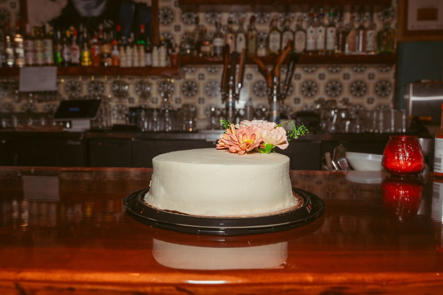 Wedding cake and bar setup at a rustic reception venue with dark wood and ambient lighting.
