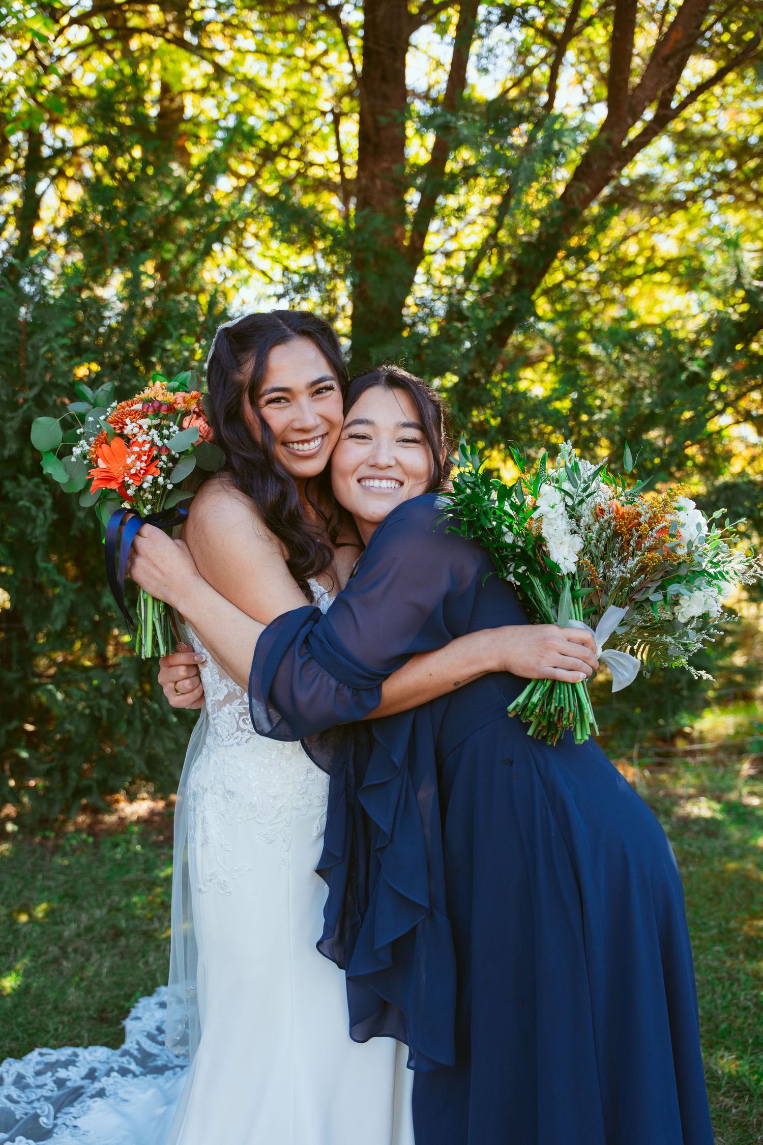 Wedding group embraces and laughs together while holding vibrant orange and white bouquets.
