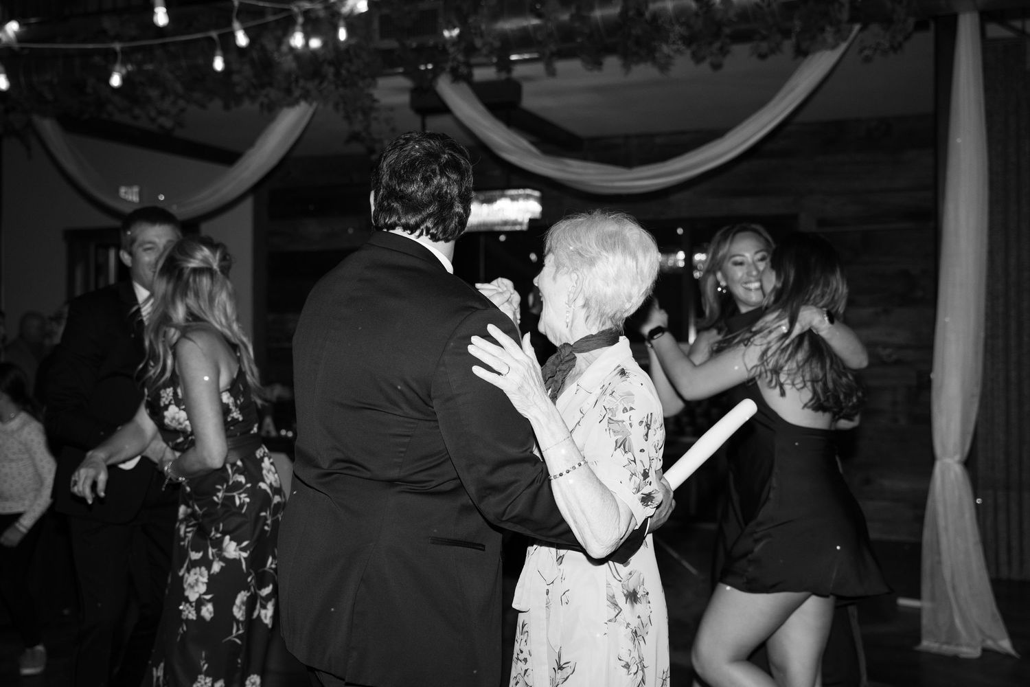 Dancers enjoying themselves under string lights and white fabric draping at an indoor venue.