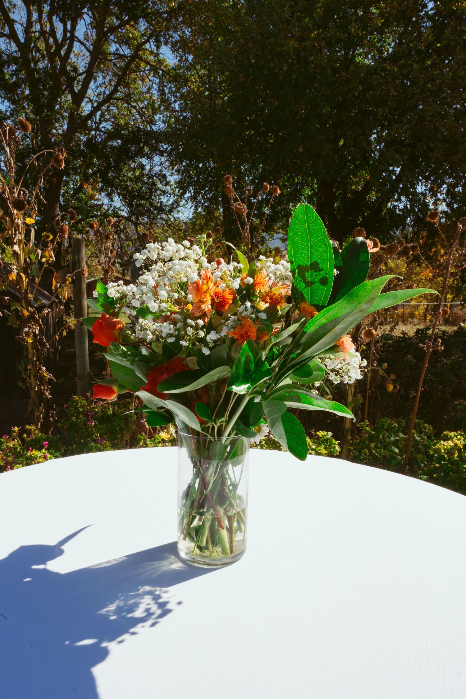 Fresh floral arrangement with white and orange flowers in glass vase on white table outdoors.