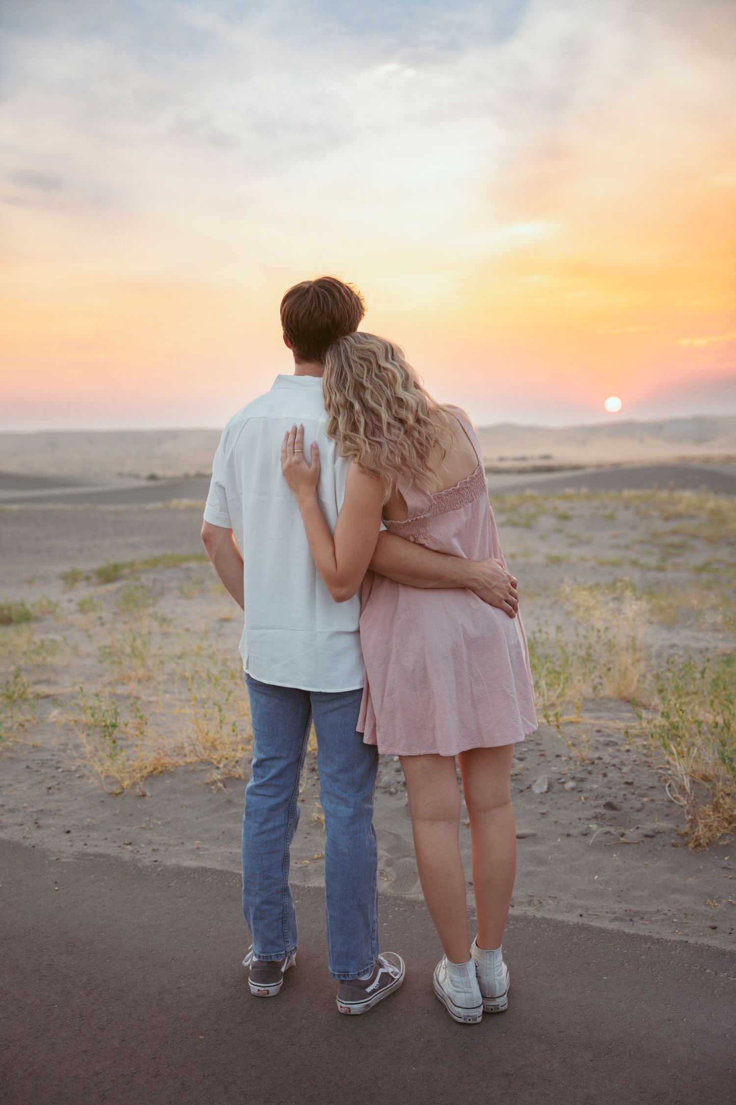 A couple stands together watching the sunset over desert hills.