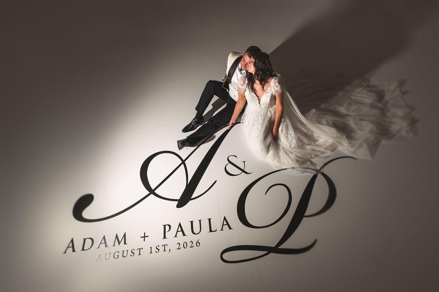 Bride and groom posing with Adam and Paula August 1st 2026 monogram light projection.