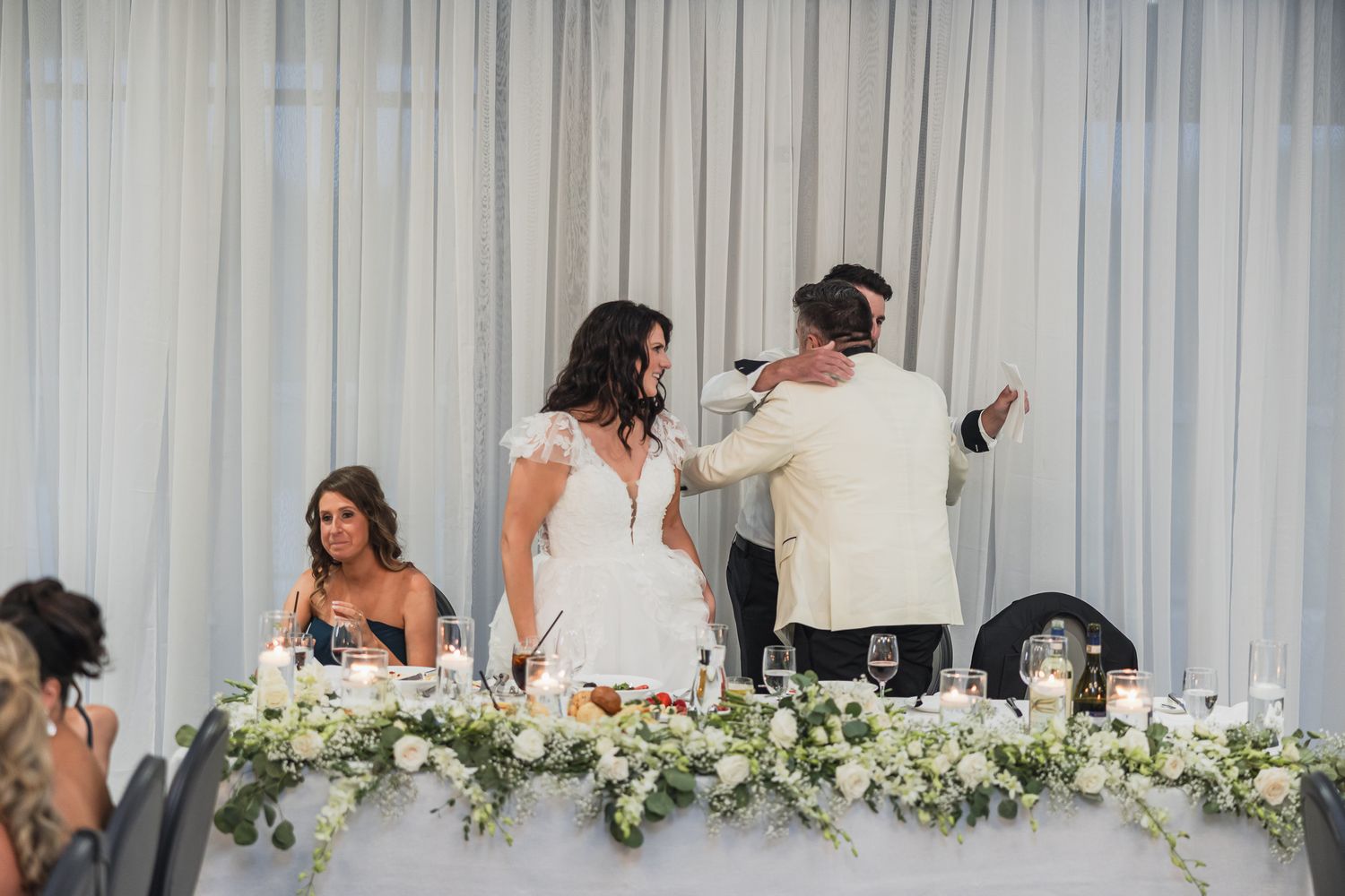 Bride and groom share a tender moment at the floral-adorned head table during wedding reception.