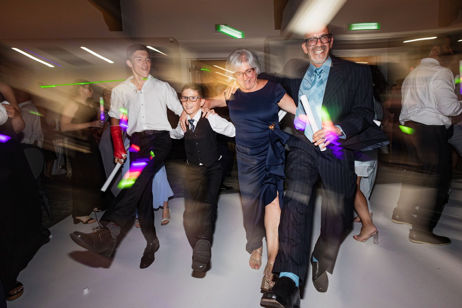 Wedding guests dancing energetically with colorful glow sticks on the dance floor.