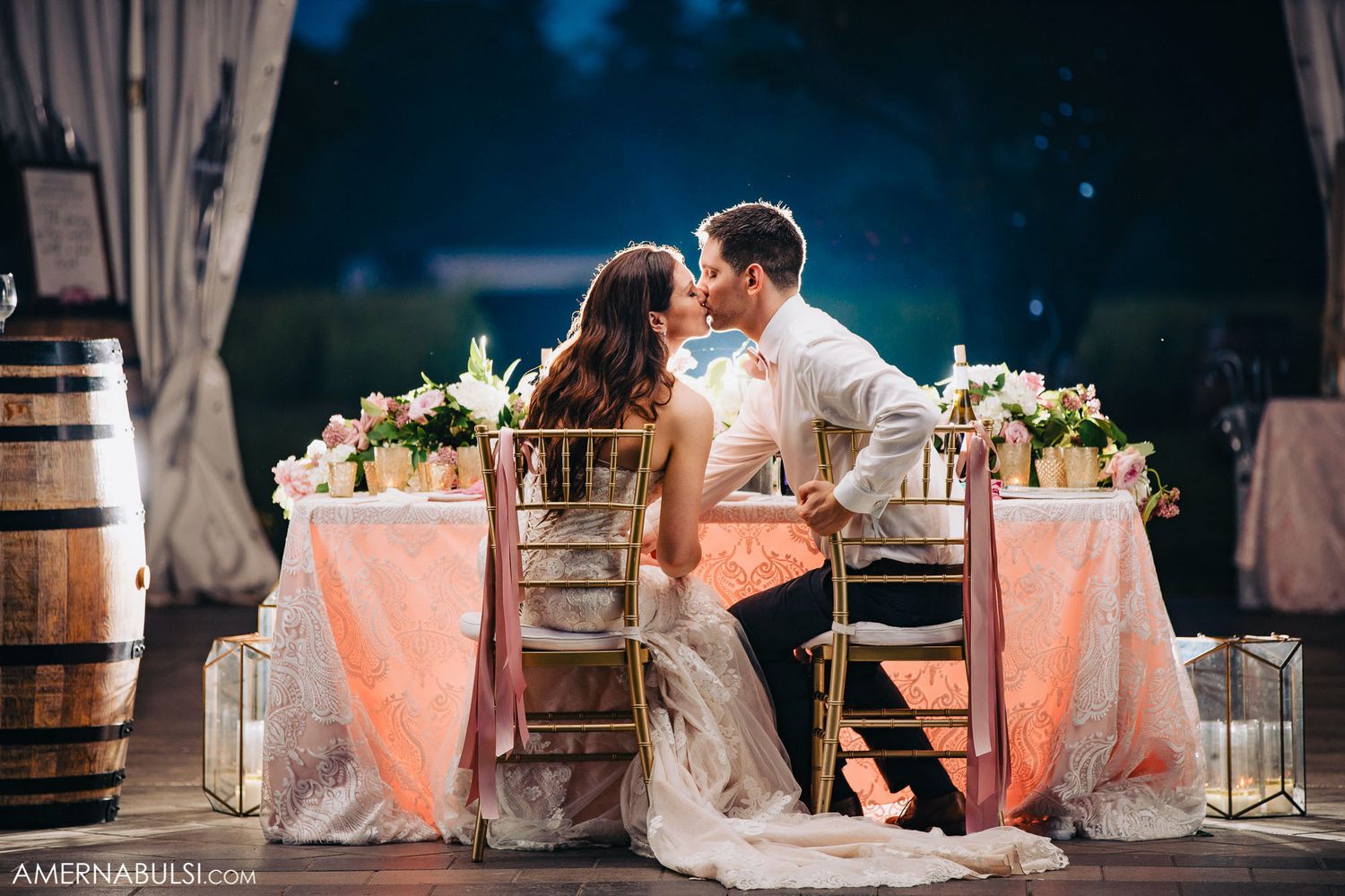 Elegant outdoor wedding reception setup with pink linens and romantic lighting at dusk.