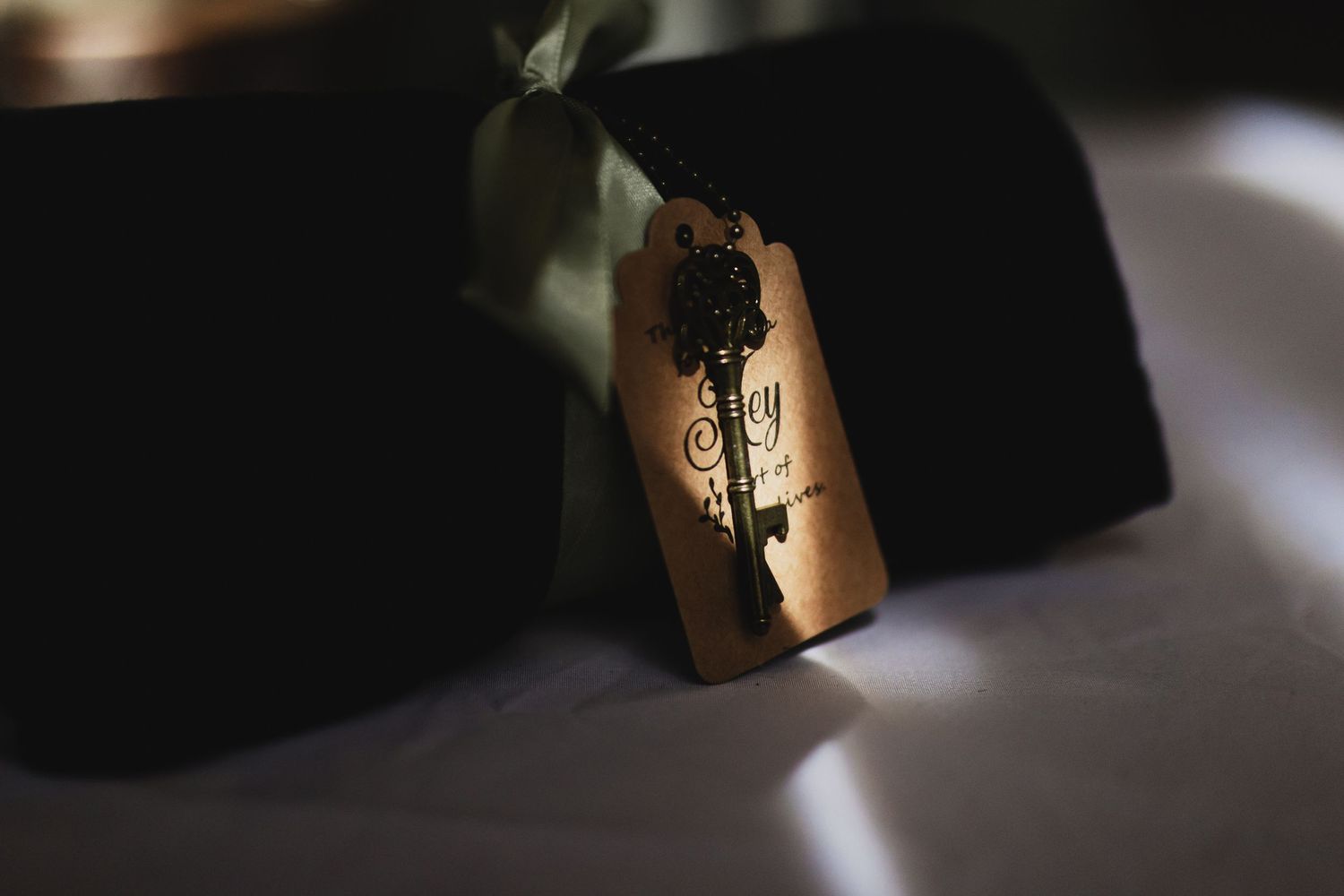 Vintage copper gift tag with ornate skeleton key charm and green ribbon on dark velvet box.