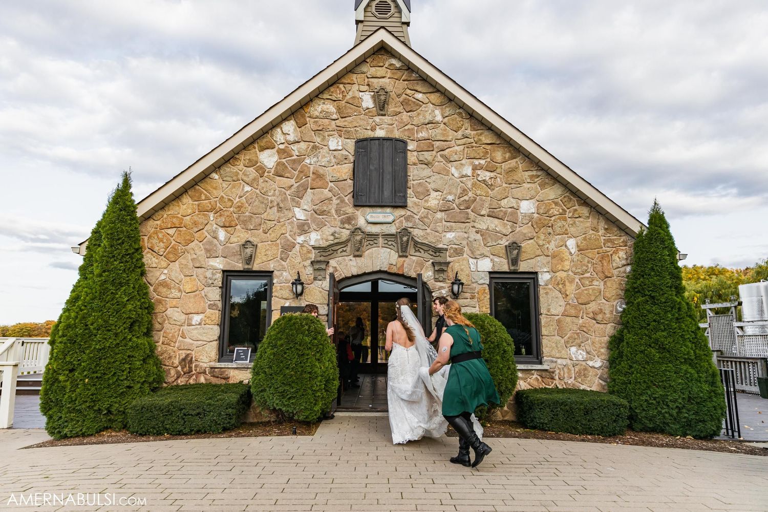 Stone chapel with manicured topiary shrubs flanking entrance during a wedding ceremony.