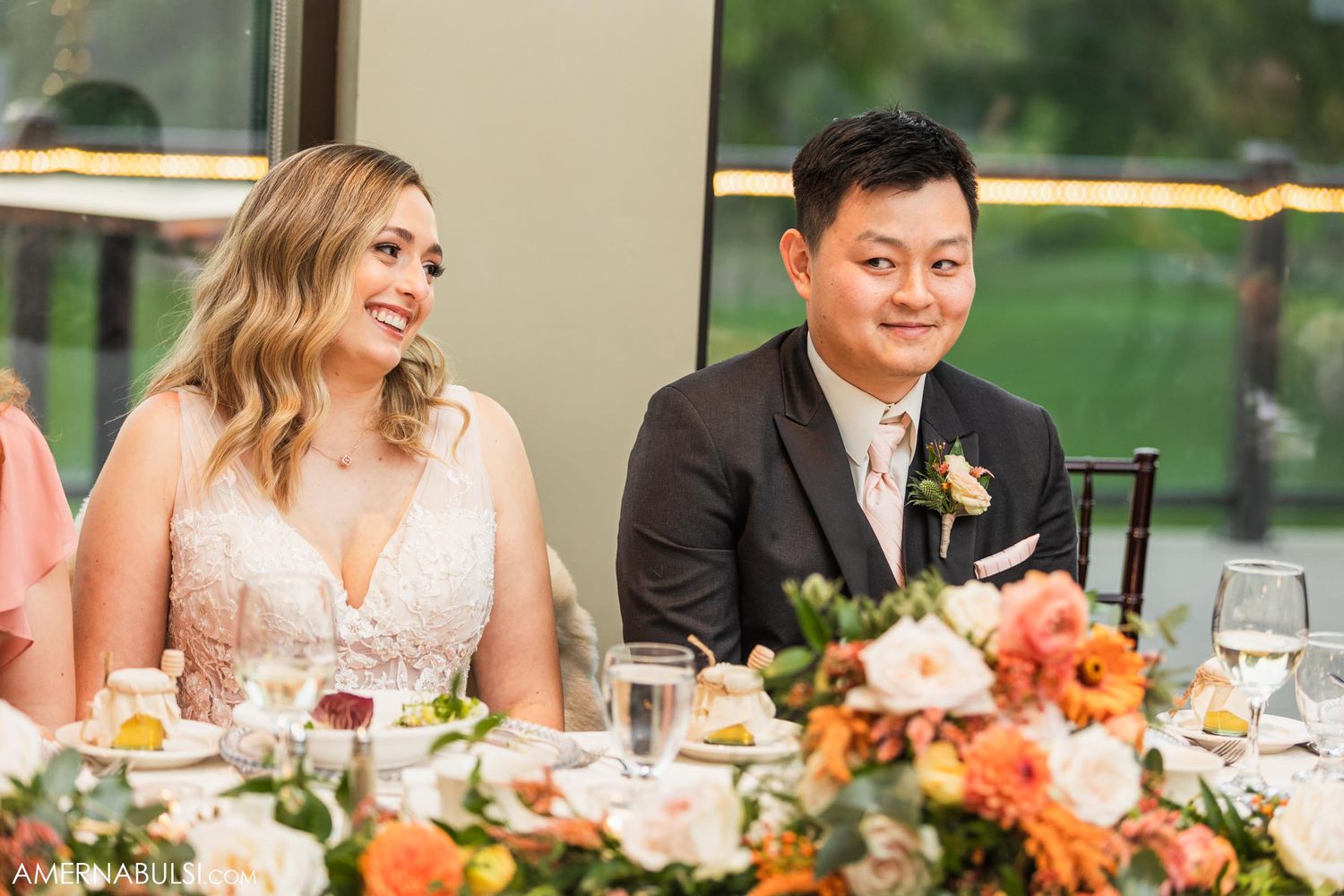 Wedding couple seated at head table with elegant floral centerpieces.
