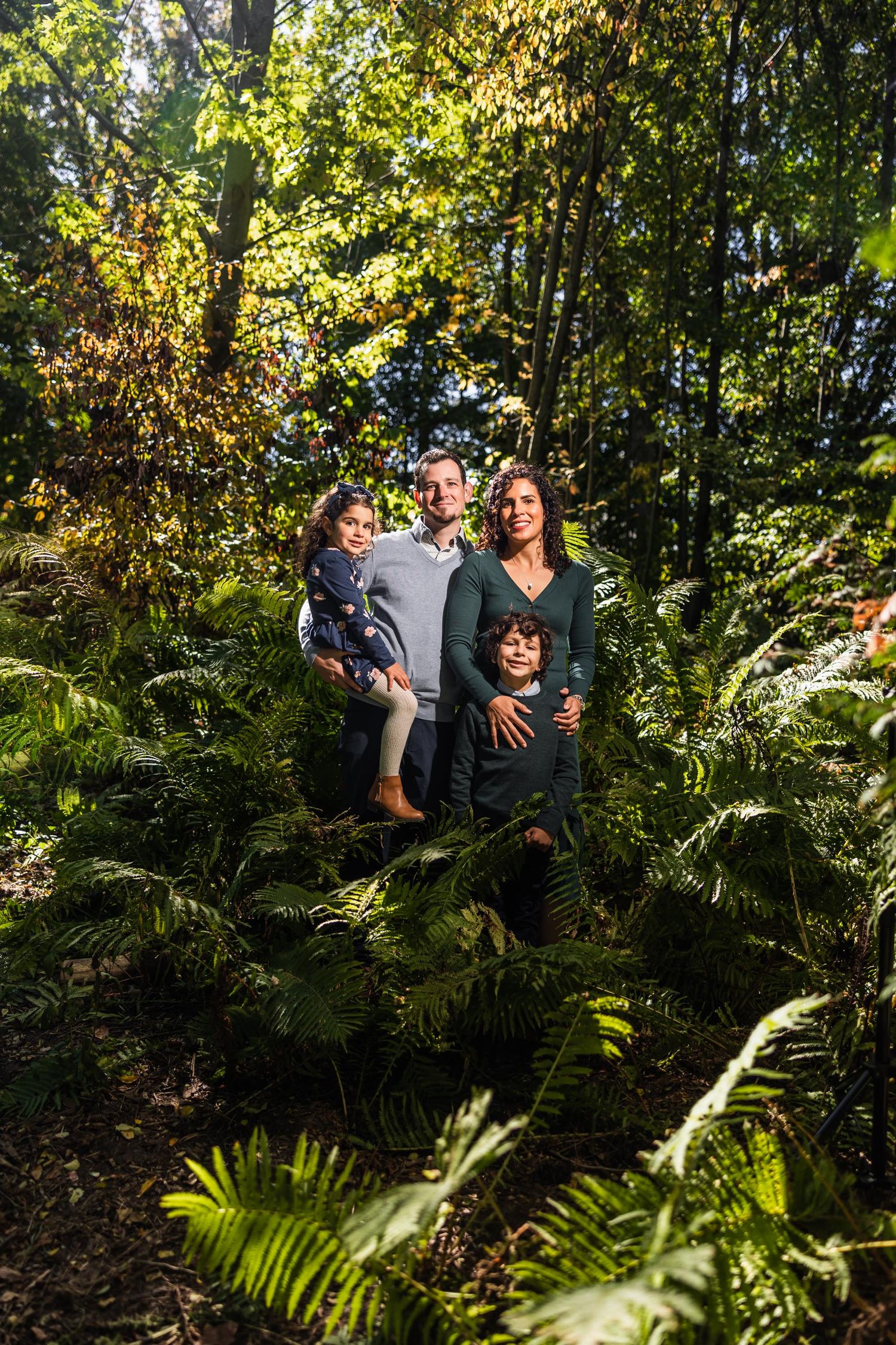 A happy family posing together in a lush green forest setting with ferns.