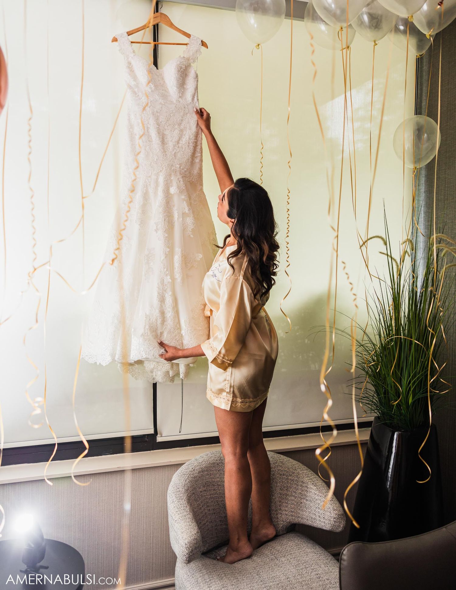 White lace wedding dress hangs elegantly among scattered balloons and ribbons.