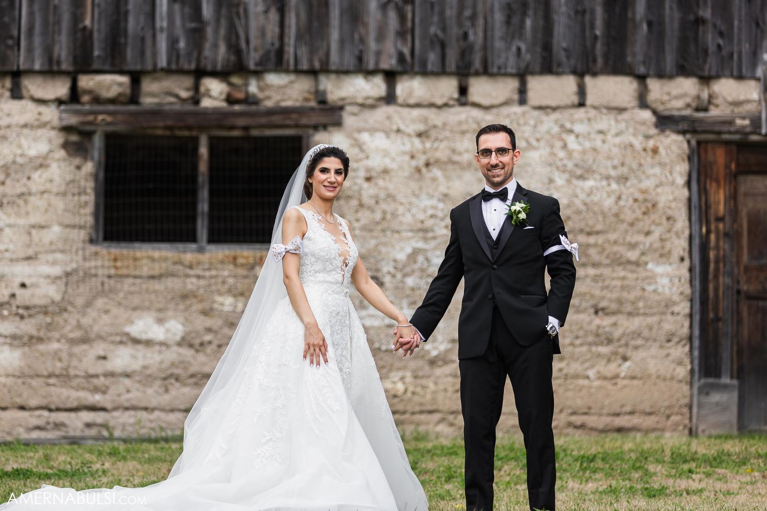 Elegant wedding couple poses together on their special day against rustic stone wall background.