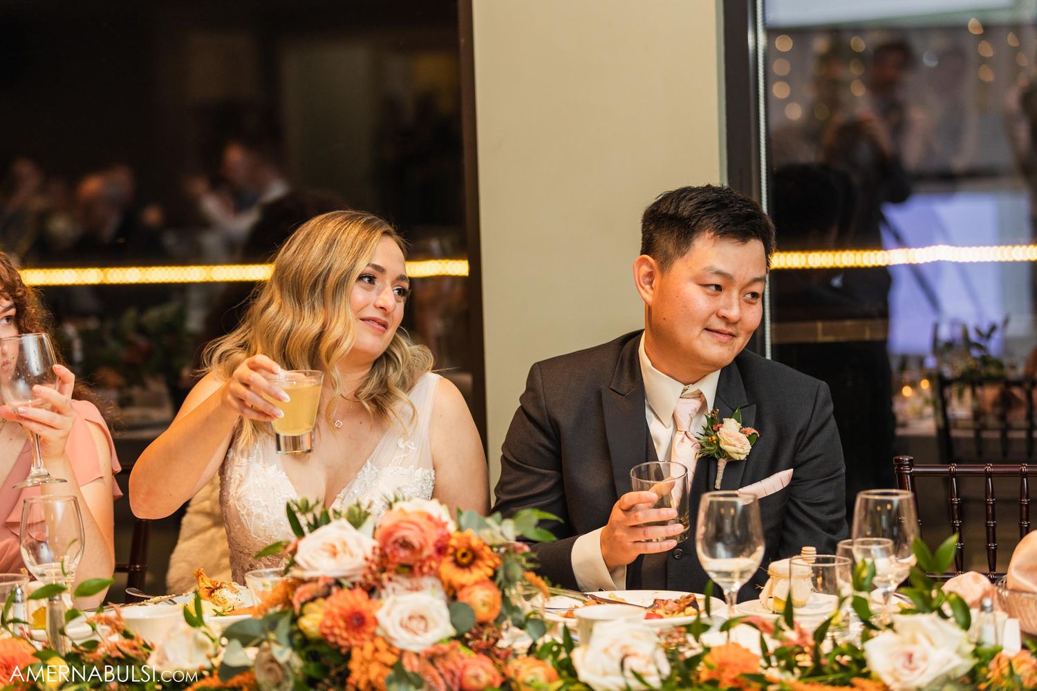 Couple sitting at decorated head table with elegant floral centerpieces during wedding reception.