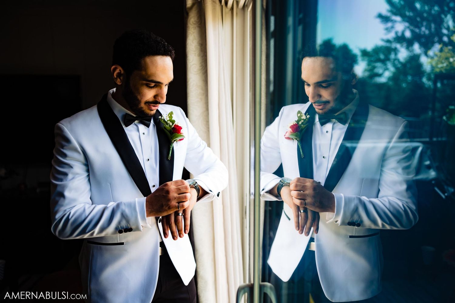 A person in a white tuxedo adjusts their attire while looking in a reflection.