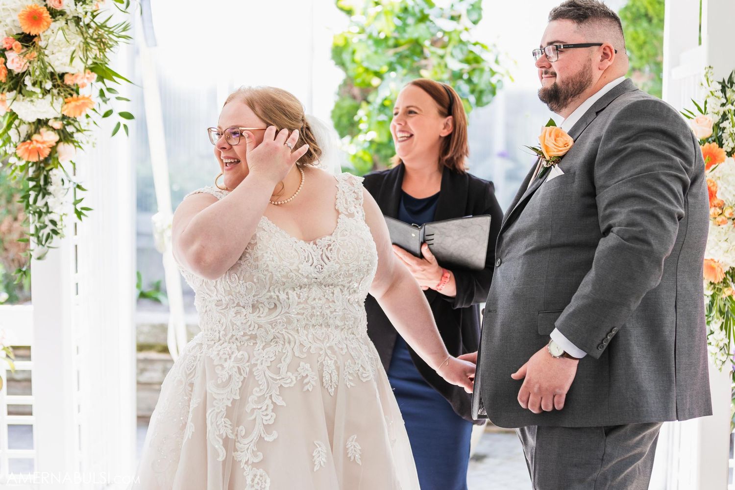 Emotional moment during outdoor wedding ceremony with officiant under floral arch.