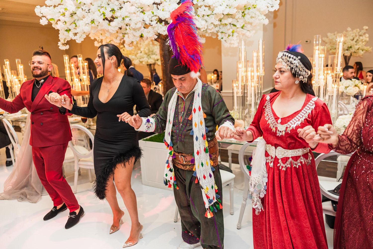 Wedding guests dancing and celebrating in formal attire with festive red feathers and decorative costumes.