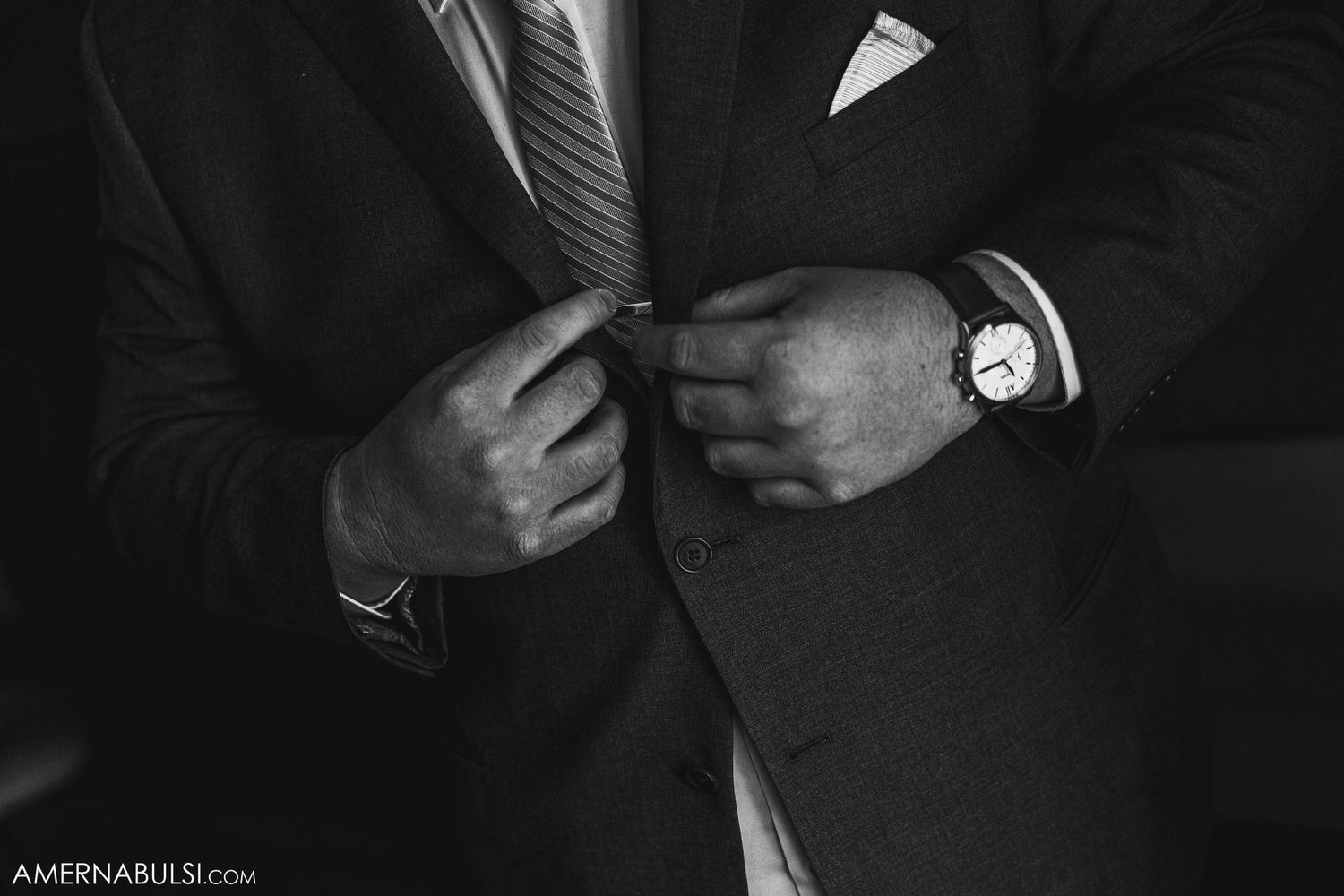 Close-up black and white shot of a groom adjusting his suit and cufflinks.