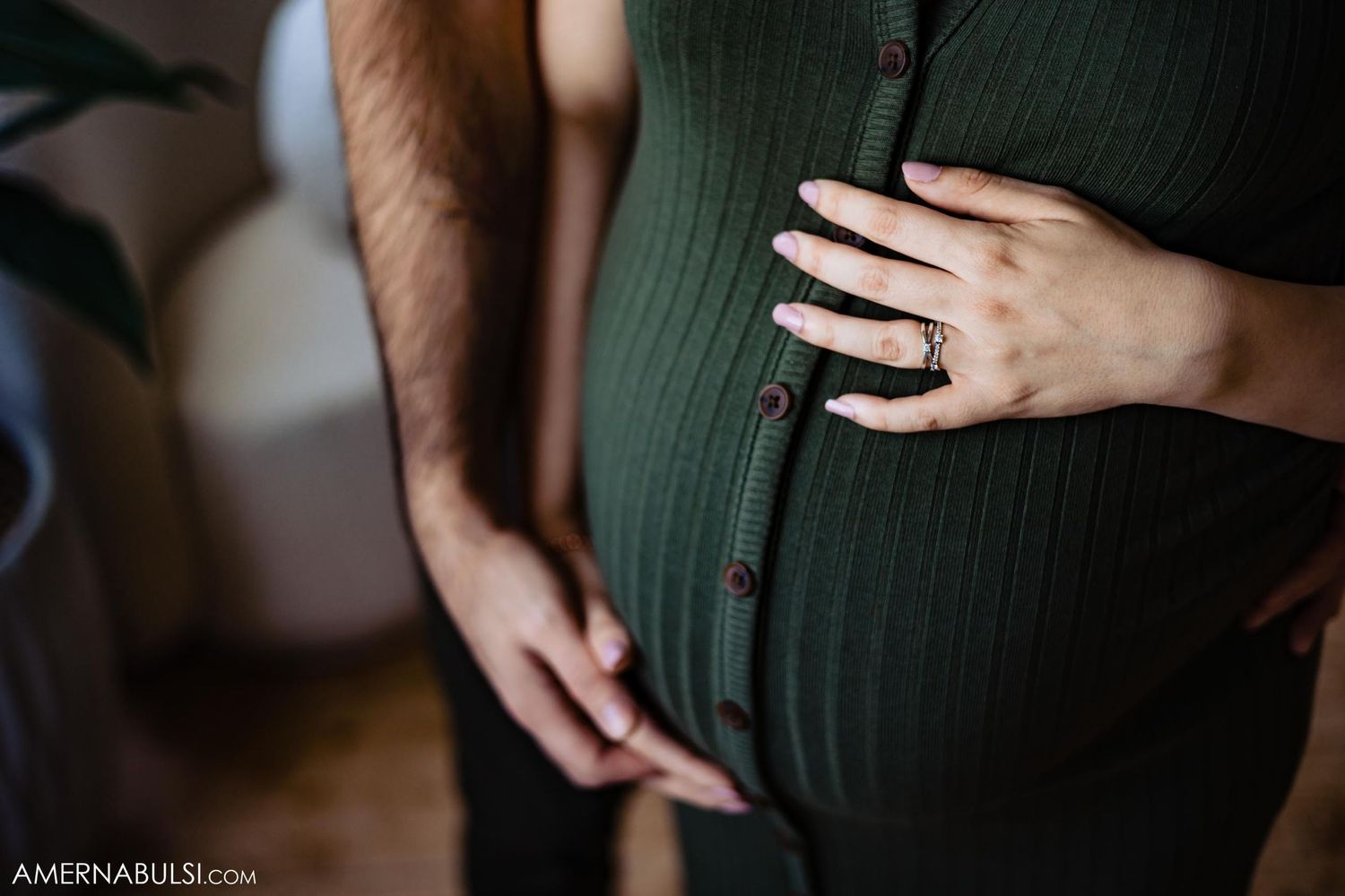 Close-up detail shot of hands resting on green ribbed maternity dress.