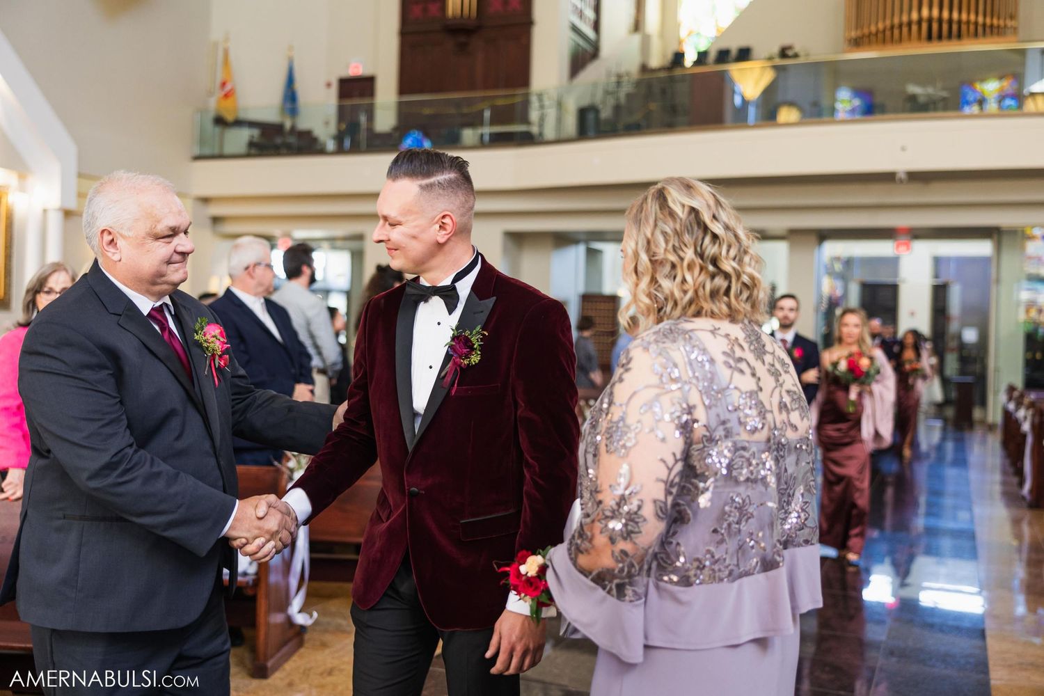 Wedding guests in formal attire greeting inside ornate church interior.