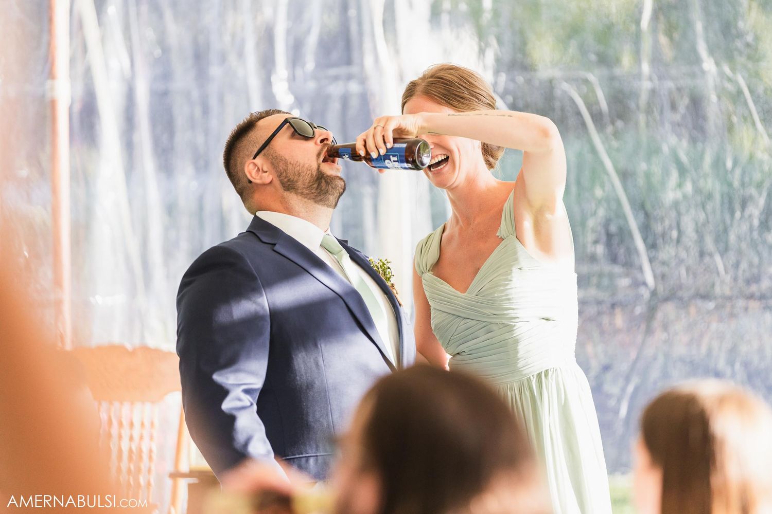 Couple sharing a playful moment with drinks during outdoor wedding reception.
