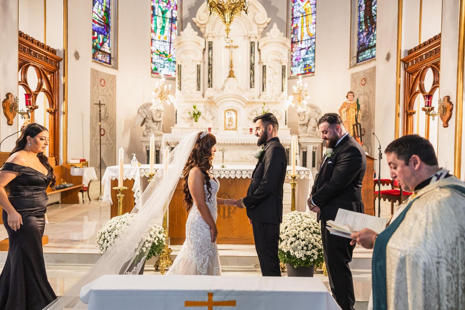 A wedding ceremony unfolds at the altar of a beautiful church with stained glass windows and ornate decorations.