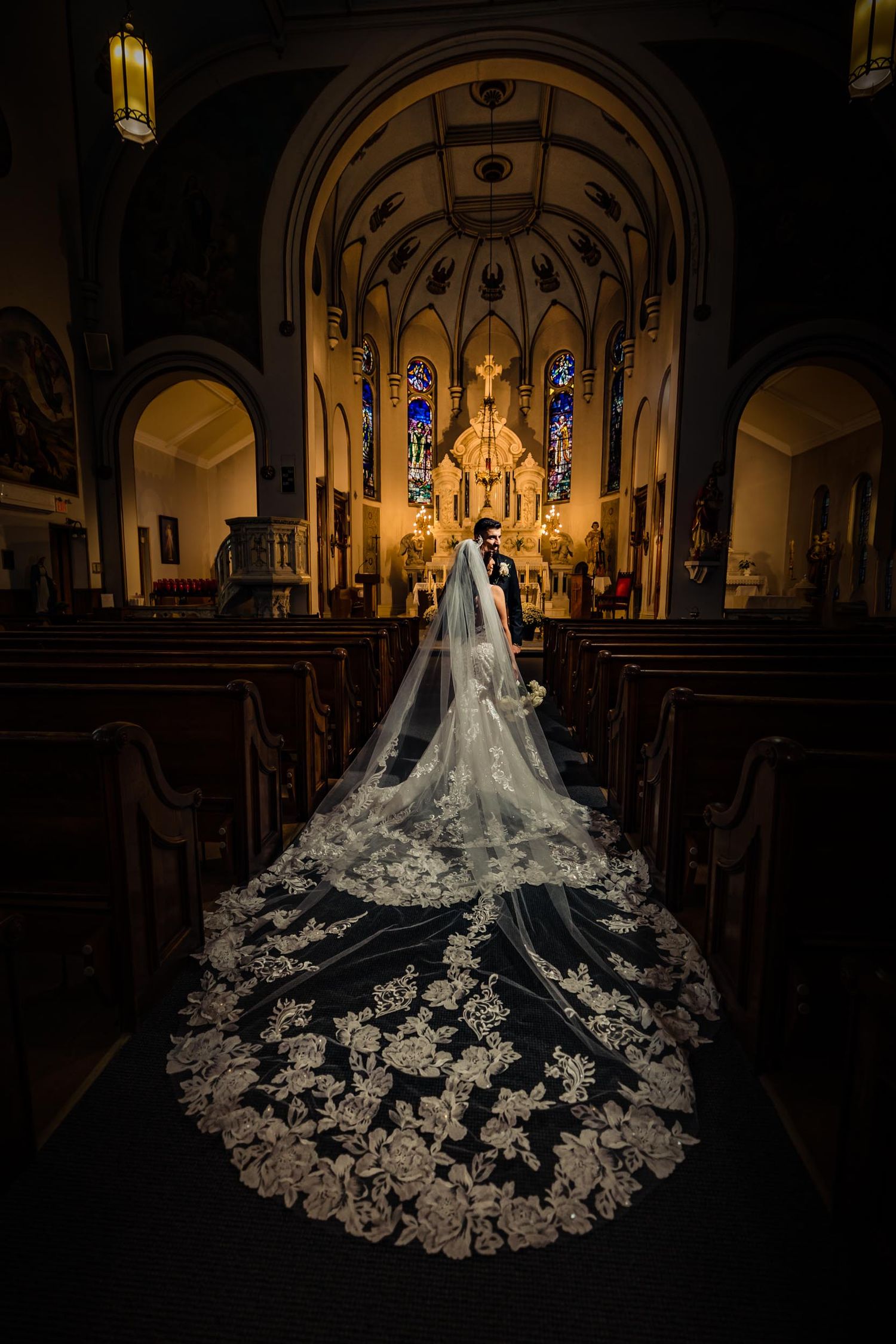 Dramatic cathedral wedding photo showing long lace veil trailing down church aisle.