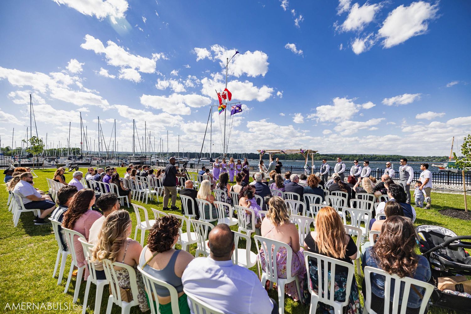 Guests seated at waterfront wedding ceremony with marina and balloons in background.