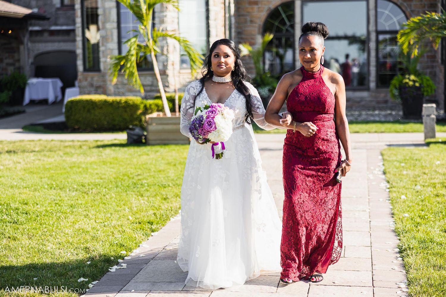 Wedding procession on garden pathway with person in white gown and red formal dress.