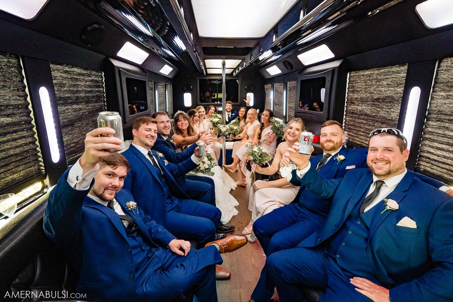 Wedding party in navy blue suits celebrating inside a luxury party bus with champagne glasses raised.
