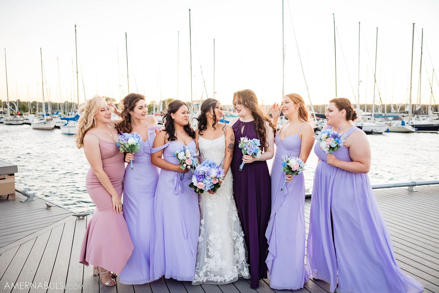 Bridal group in purple and pink dresses holding bouquets at marina.