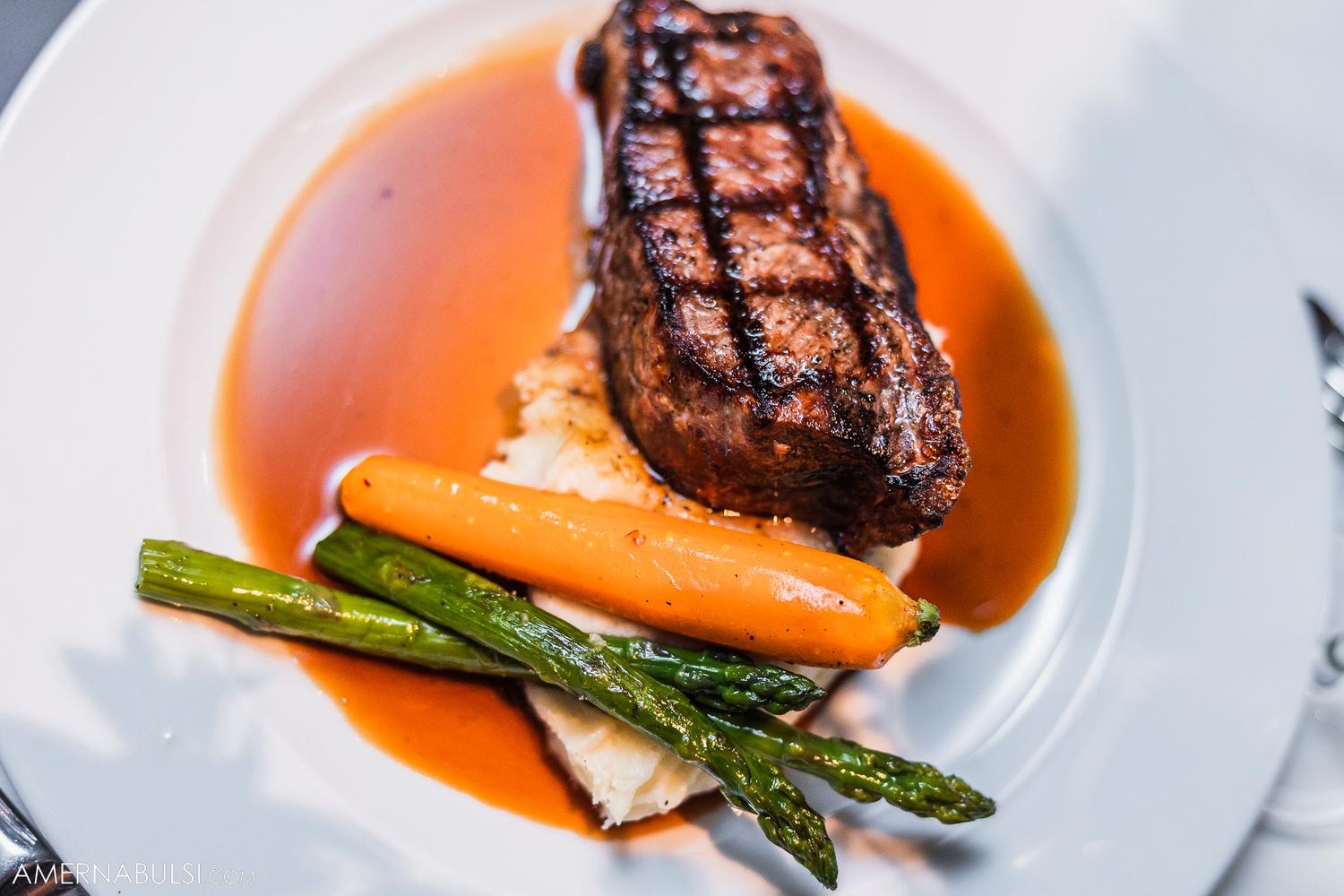 Grilled steak with asparagus and carrots in orange sauce on white plate.