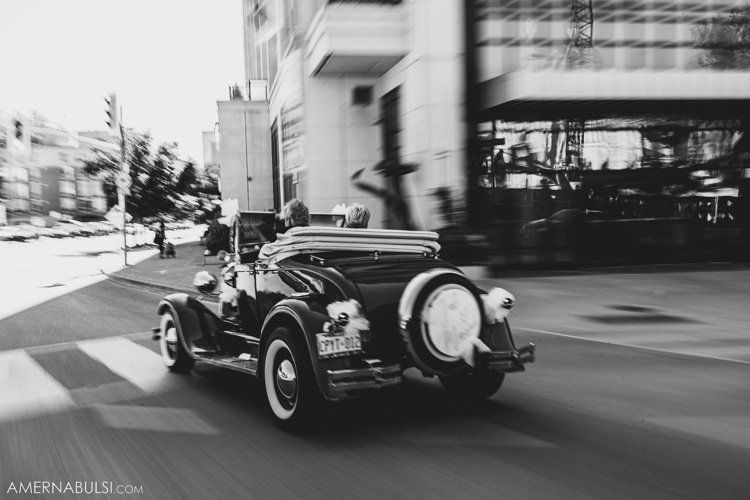 Motion blur shot of a vintage black convertible car driving on a city street.