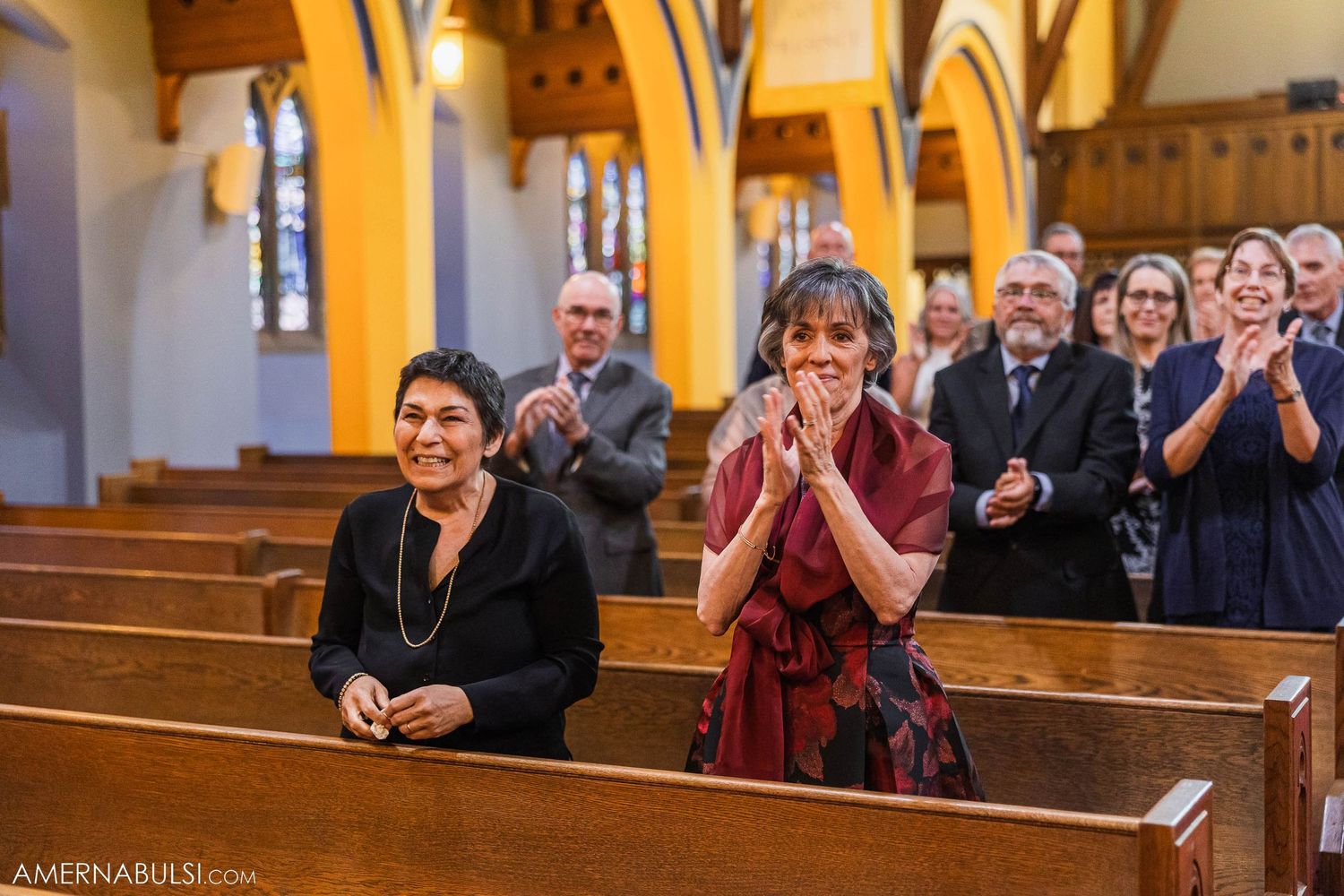 A couple walks down the aisle during their wedding ceremony in a beautiful church with stained glass windows.