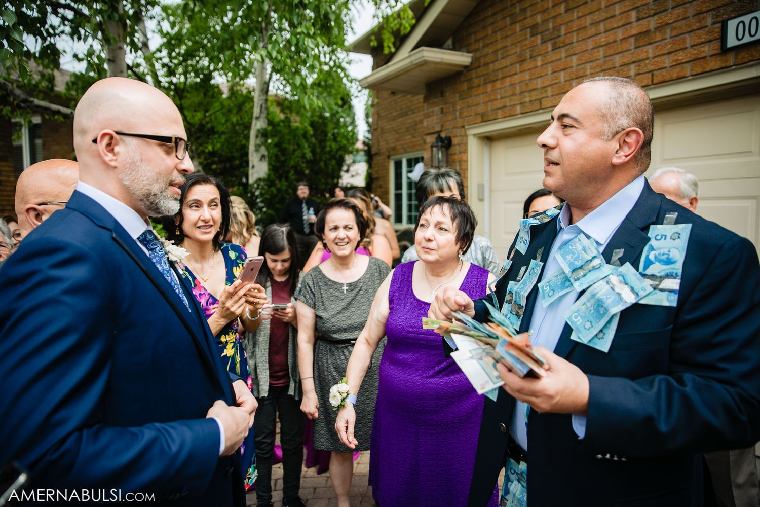 Wedding guests mingle and socialize during an outdoor reception near a brick building.
