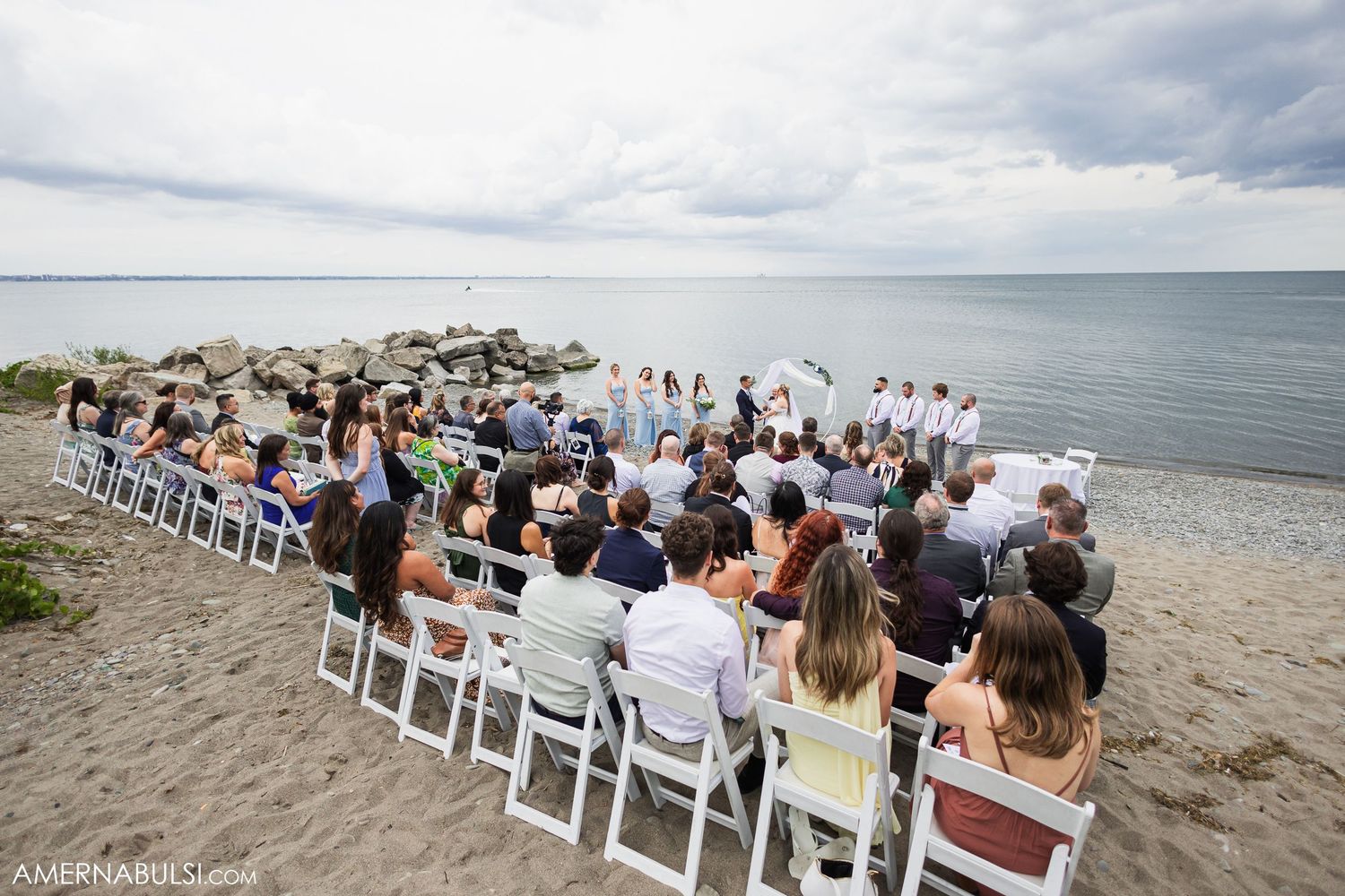 Beach wedding ceremony setup with rows of white chairs and guests facing the ocean.