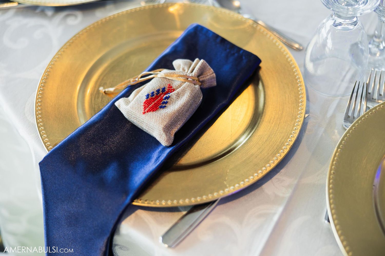 Gold charger plate with navy blue napkin and decorative favor bag at wedding place setting.