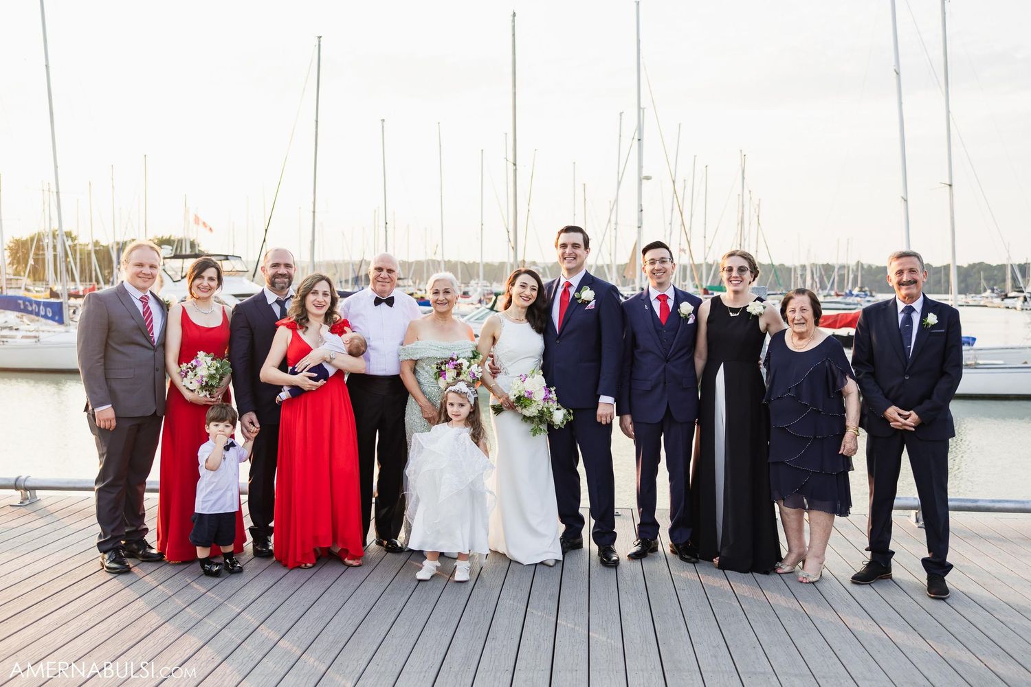 Large wedding party group photo on a marina dock with boats in background.