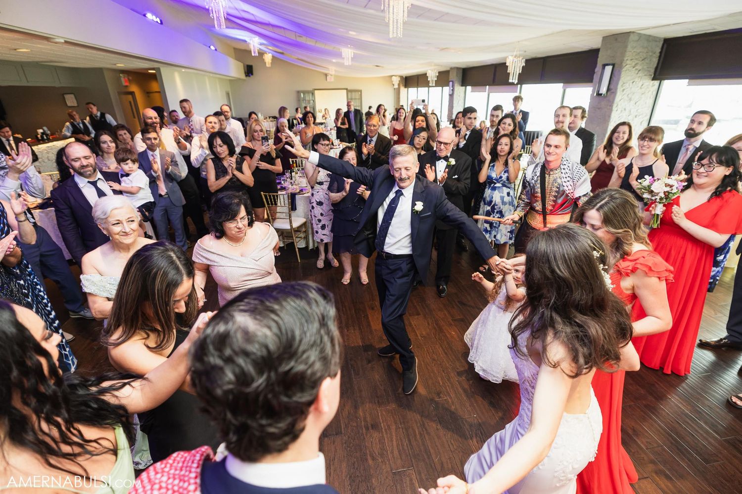 Wedding celebration with crowd gathered on dance floor under purple lighting.