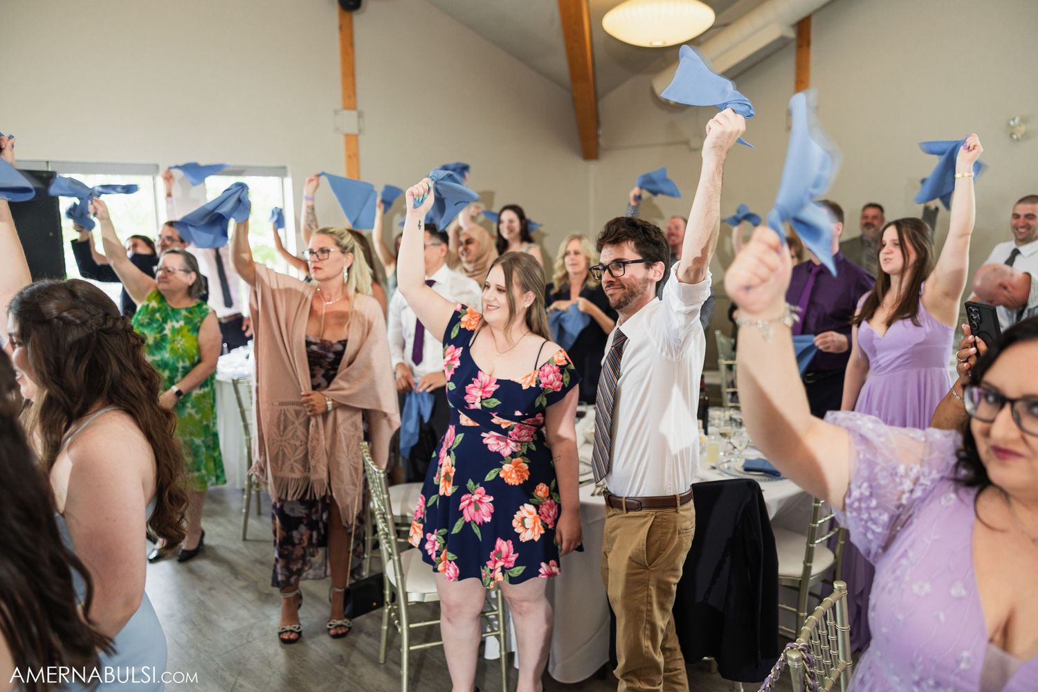 Wedding reception guests dancing and celebrating with hands raised in a bright indoor venue.