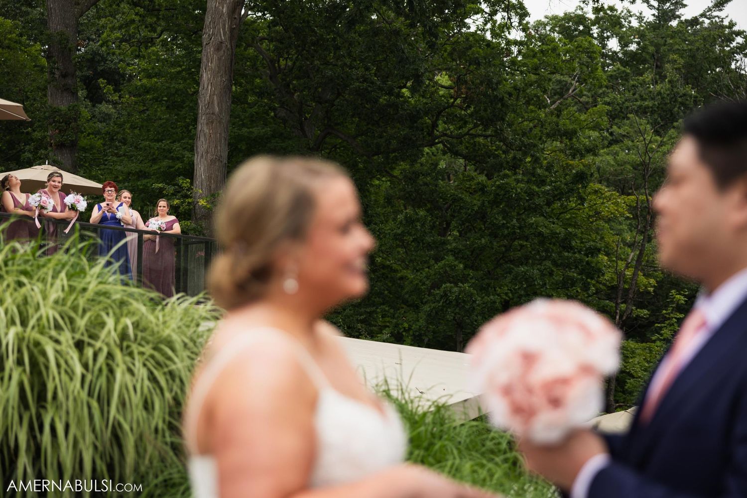 Wedding couple sharing a moment in a garden setting with guests visible in background.
